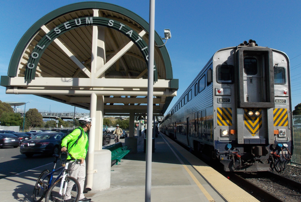 Bicyclist watches Capitol Corridor train pull into Coliseum Amtrak station.