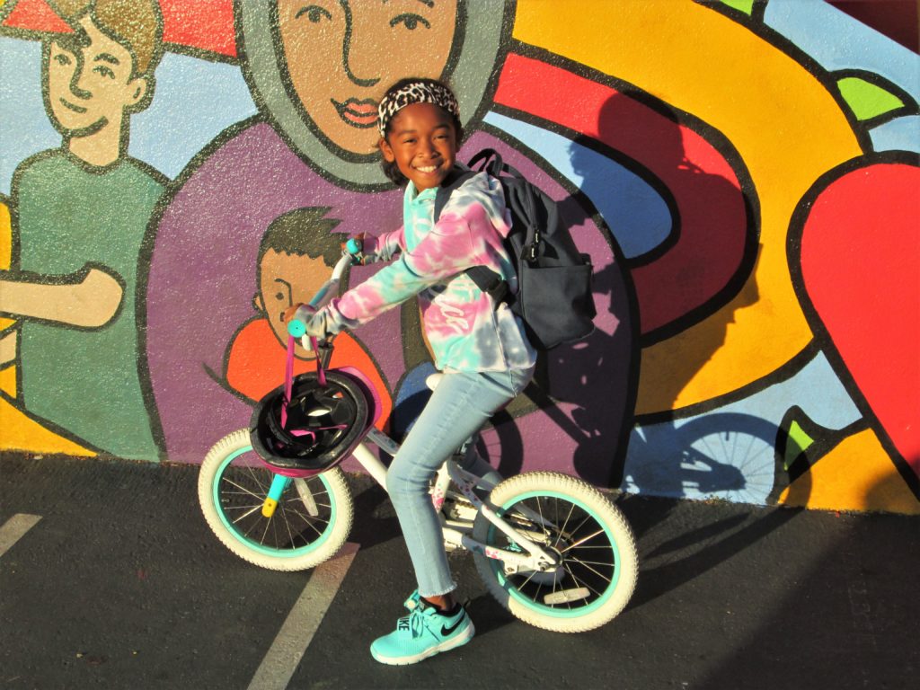 An image of a child on her bike in front of a mural. 