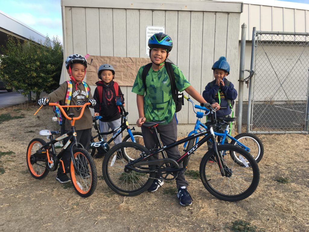 An image of four children with their bicycles outdoors. 