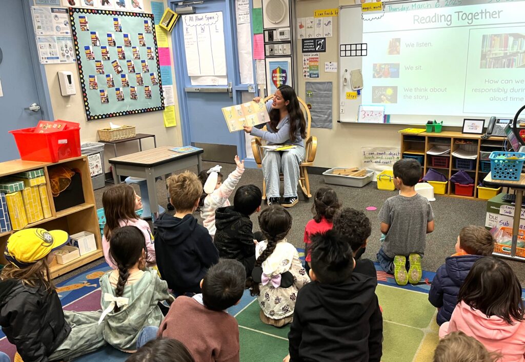 A high school students reads a book to a classroom of elementary school students